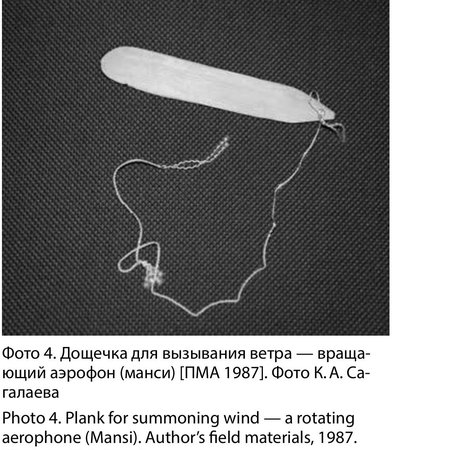 A pale, gently tapered Mansi wind-summoning plank photographed loose on its long looped cord, field photograph from 1987 — the instrument...