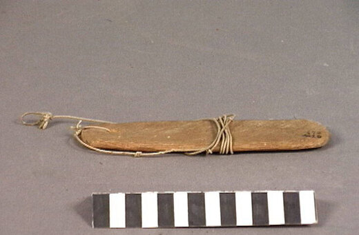 The Aruba zeeuw itself: a roughly worked oval wooden plate with its long cord still looped and wound around the blade.