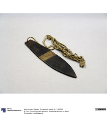 A dark wooden blade with a pale diagonal band painted across its middle, a coil of plant-fibre cord bound at the pierced end — the Nahukuá...