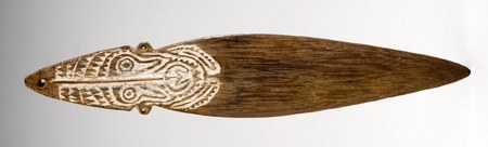 The Kaimari Island bull-roarer itself: a lime-whitened spirit face carved into the dark palmwood blade, cord hole at the tip of its head.