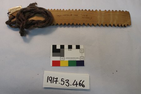 Saw-toothed wooden srannan with its wound wool cord and tie-on label, Scotland.