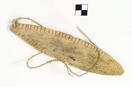 Southampton Island bone blade with evenly spaced notches along both long edges; a twisted sinew cord is looped through its end hole.