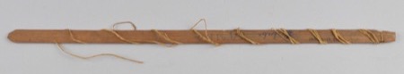 A long, narrow wooden slat with cord bound at several points along its shaft and an old accession number inked near one end — a Luba...