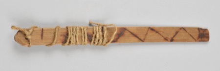 An African bull-roarer cut from a pale flat strip of bamboo, twine wound in loose coils around its upper half and a scorched zigzag line...