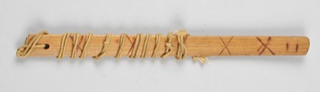 A wooden board burned with crosses and cross-hatching along its length, cord wound repeatedly near the perforated end: an African bullroarer of...