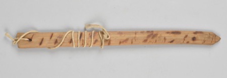 A wooden board marked with scattered burned dashes, cord wound near one end: an African bullroarer of the general type, not the Wagenia (Genya)...