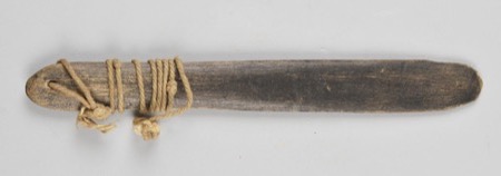 A dark wooden board bound with cord near its perforated end: an African bullroarer of the general type, not the Bakumu (Komo) instrument...