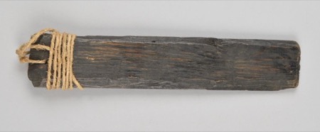 A narrow rectangular board of blackened, weather-grained wood, entirely undecorated, pale twine wound in tight coils around one squared end: an...