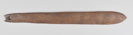 A plain wooden blade, its narrow end cut into a stepped tang pierced by a small rectangular hole, the other end tapering to a rounded point — a...