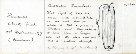 The museum's own accession card for this piece - a flat object of hard red wood pierced at one end for a twisted cord, noted on registration as...