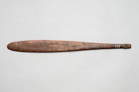 An Island Melanesian bull-roarer carved with wavy zigzag bands and a small round-eyed, toothed face near one tip — a Banks Islands piece from...
