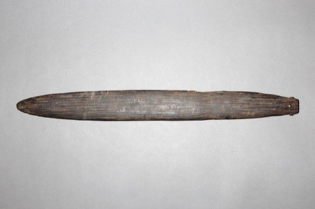 A plain wooden blade of dark, strongly grained wood, one end drawn out into a small hooked tip with a drilled cord hole - an Island Melanesian...