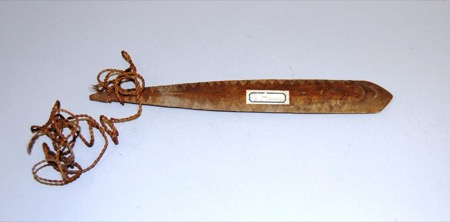 A New Guinea bull-roarer carved with a zigzag chevron border down one edge, its cord wound in a loose coil at the narrow end; a general Sahul...