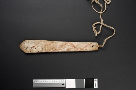 A weathered Hopi bull-roarer with faint red diagonal paint bands and a fibre cord through the perforated end; the Coast Miwok umul recorded by...