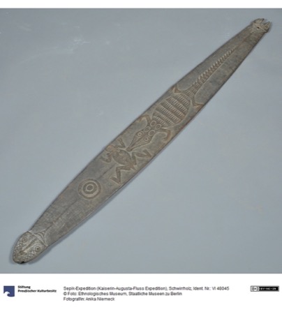 A similarly carved New Guinea bull-roarer with a small animal head at each tip, the upper blade incised with a hatched fish-like panel, a...
