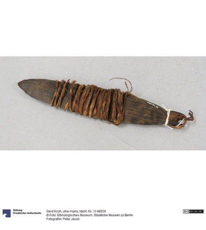 A dark, undecorated bull-roarer blade, pointed at the tip, with a thick hank of bast cord wound many times around its middle and trailing off...