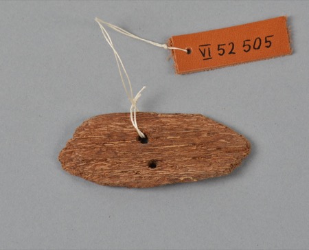 An Eipo bull-roarer, a small weathered slip of wood pierced with two holes and hung from a museum thread; not the Wampar object documented here.