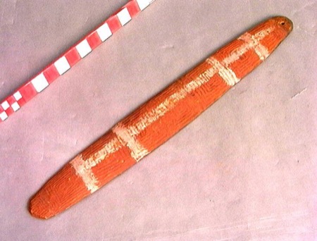 A bright red-ochred Aboriginal Australian bullroarer crossed by four white painted bands, the topmost just under the tip, its finely striated...