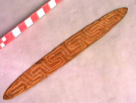 A board carved edge to edge with a herringbone zigzag pattern — an Aboriginal Australian bull-roarer held by the Wereldmuseum, shown for the...