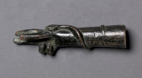 A small Roman bronze votive forearm and hand raised in blessing, with a snake coiled along the wrist and forearm, its head resting on the back of the hand.