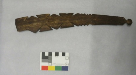 A dark wood blade cut with bold diamond-and-cross openwork and runs of saw-tooth serration along its middle, tapering to a small knob at the...