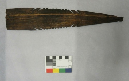 Another notched, saw-toothed wood blade of the same Naga type, blackened with age and tapering to a narrow tail where only a wisp of thread...