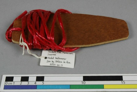 Another Pitt Rivers model bullroarer, the same oval board type wound this time with red cord — a stand-in for the Scottish 'thunder-spell,' no...