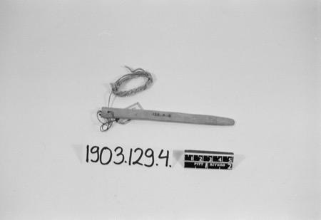 A slender wooden stick with a coiled cord, photographed with its Pitt Rivers catalog card 1903.129.4.1 - a Zuni piece shown for the general...