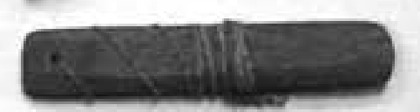 Black-and-white photograph of a flat bone strip with a hole near the left end, several incised bands and a rounded right tip.