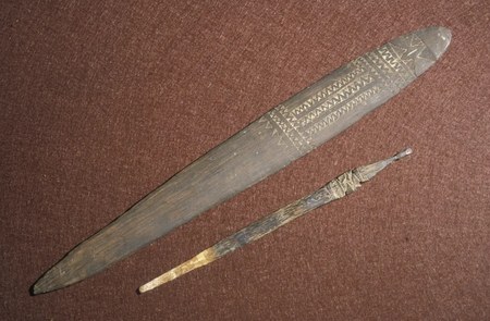 A flat wooden blade incised near one rounded end with rows of small banded triangles below a star-like figure, its tips plain and unpierced, a...