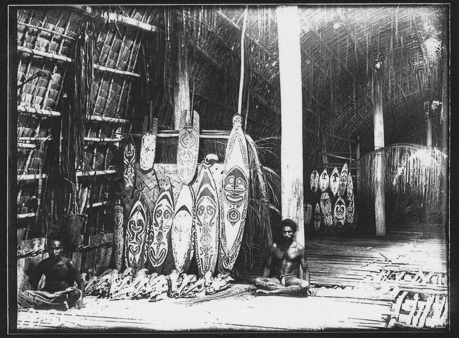 Two men sit beside painted face boards and a row of animal skulls inside Onopo Ravi.